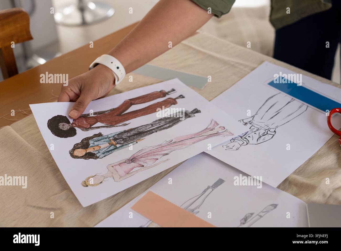 Feuille de croquis de mode occupant le centre de la table de travail en tissu beige, avec ciseaux et règle à proximité Banque D'Images