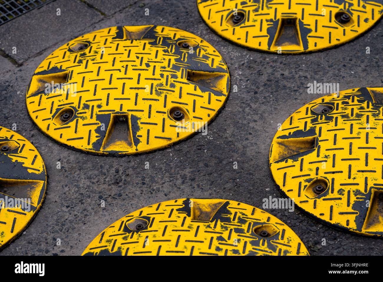 Close-up de ralentisseurs circulaires jaunes avec des marquages noirs fortement usés sur un asphalte rugueux, créant une composition abstraite frappante de couleur et de texture Banque D'Images