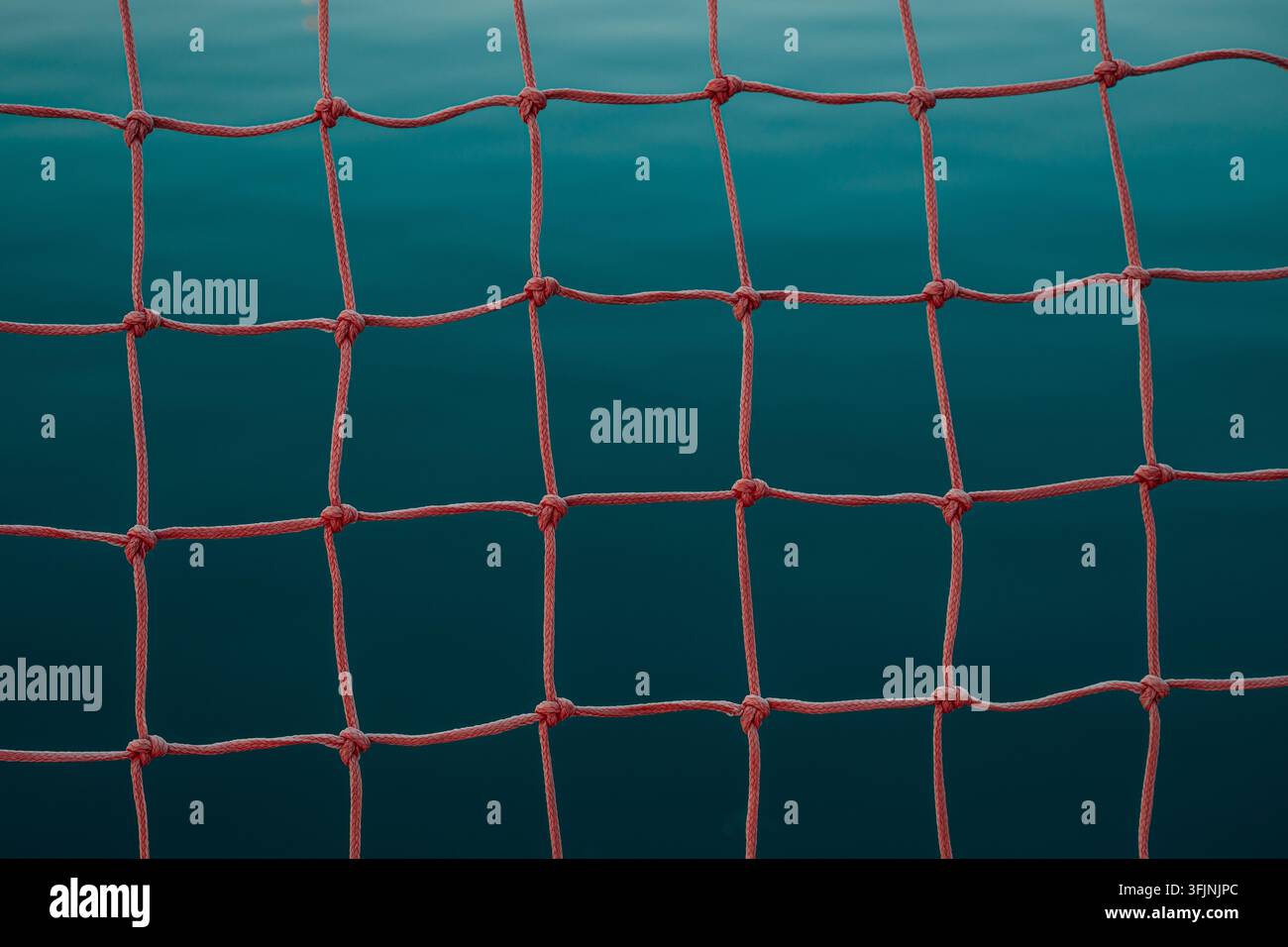 Texture de filet sportif rouge sur l'eau calme de l'océan. Concept de water-polo, sports aquatiques compétitifs, précision et équipement sportif. Mise au point sélective. Banque D'Images