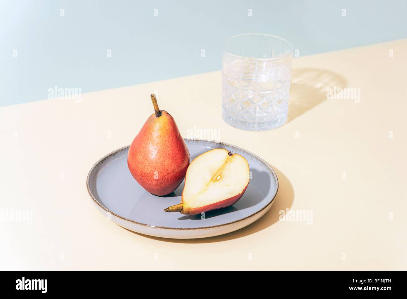 Poires dans une assiette et verre d'eau sur fond clair avec ombres. Concept automnal, gros plan. Banque D'Images