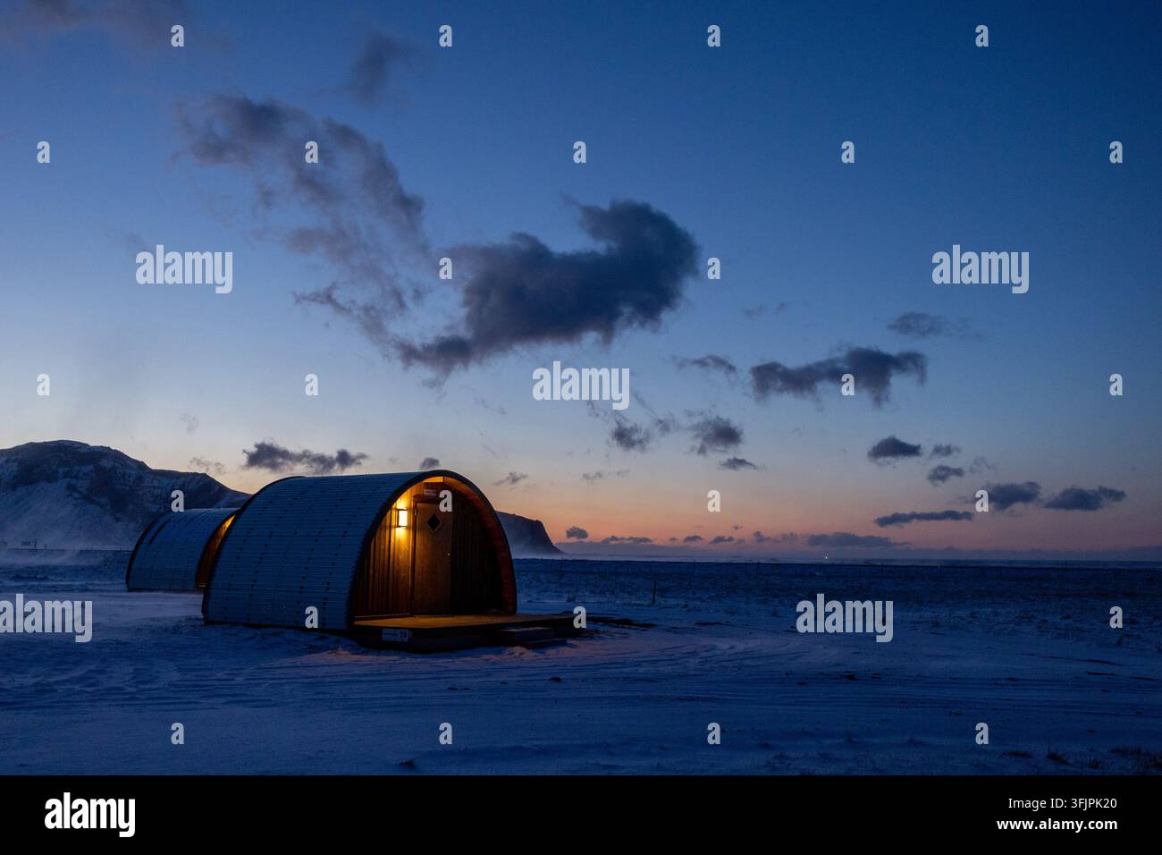 Vue de cabanes en forme de tonneau illuminées au crépuscule dans un paysage enneigé à Hvolsvollur, Rangarthing eystra, Islande. Banque D'Images