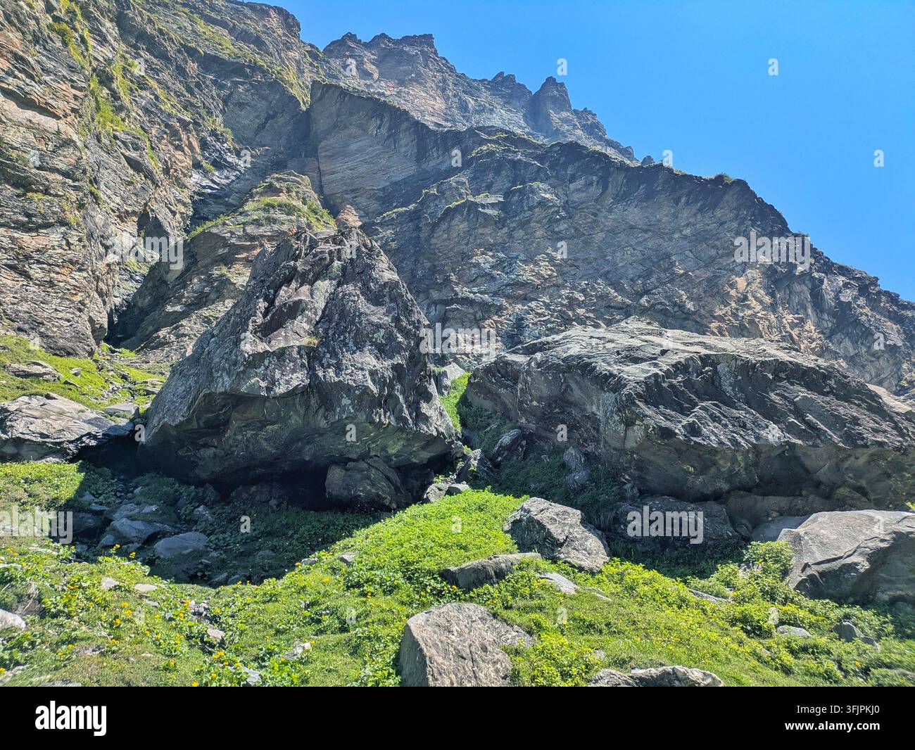 Boulder célèbre du Rocher du Tigre entouré de prairies vertes face à une immense paroi montagneuse sur le sentier de randonnée du Col Hampta, Inde - Image de stock capturée avec un smartphone