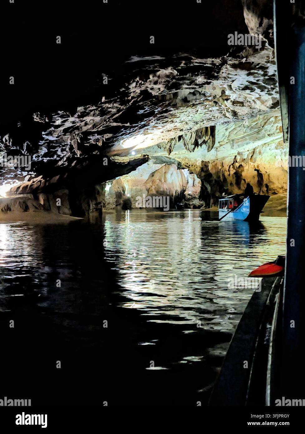 PHONG NHA, VIETNAM - 18 MARS 2026 : Bateau touristique bleu marqué PHONG NHA CAVE naviguant à travers la caverne brillamment éclairée remplie de stalactites suspendues - Image de stock capturée avec un smartphone