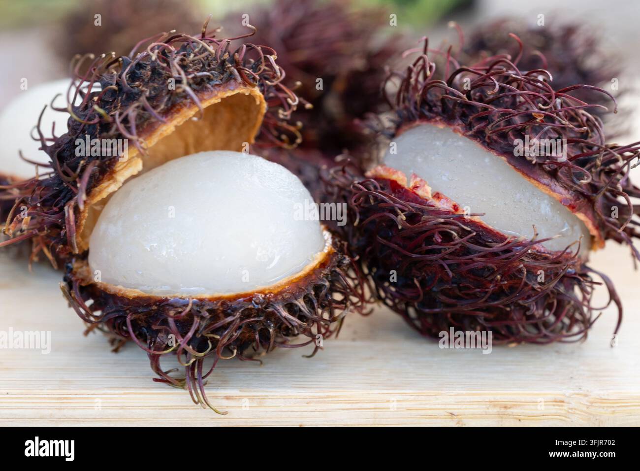 Close-up de plusieurs fruits de ramboutan ouverts disposés sur une surface en bois rustique. L'image met en valeur le contraste entre l'écorce épineuse rouge-brun et Banque D'Images