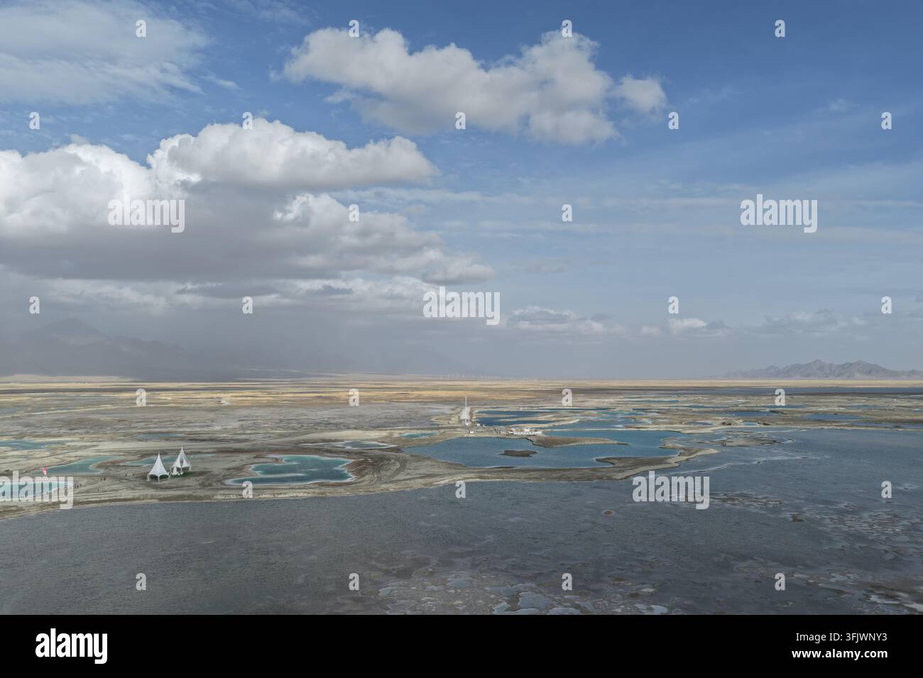 Une vaste marais salant parsemée d'innombrables petites mares s'étend vers des montagnes brumeuses sous un ciel rempli de nuages. La mosaïque d'eau et de sel remplit t Banque D'Images