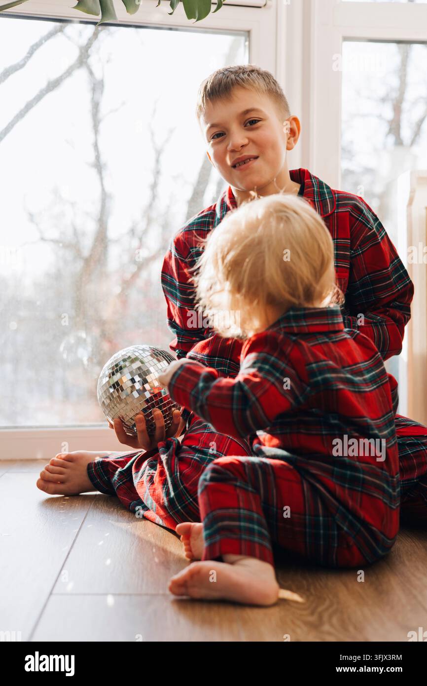 Deux frères en pyjamas à carreaux assortis jouant avec des décorations de Noël à la maison Banque D'Images