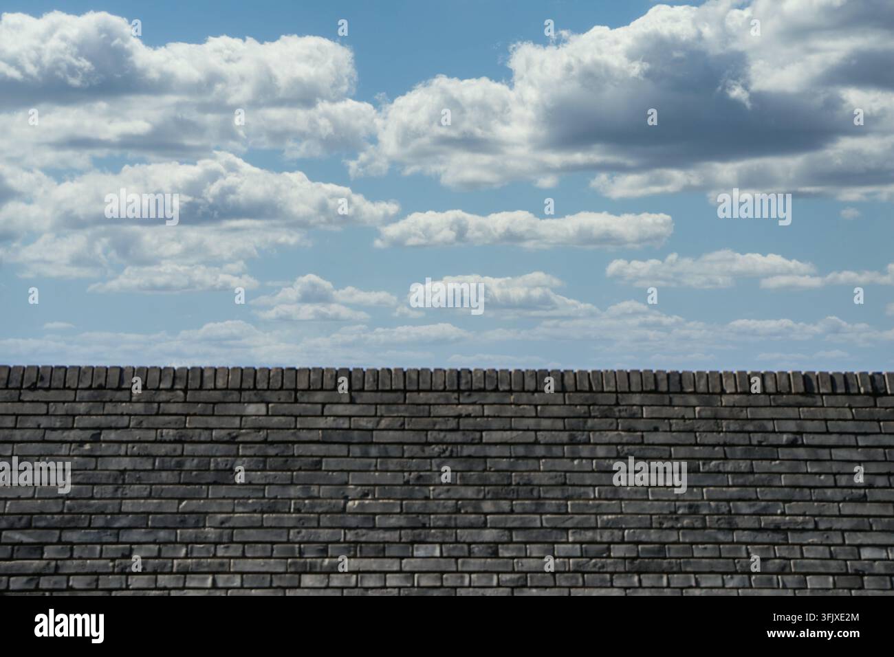Composition symétrique d'un mur de briques gris patiné et de nuages blancs superposés Banque D'Images