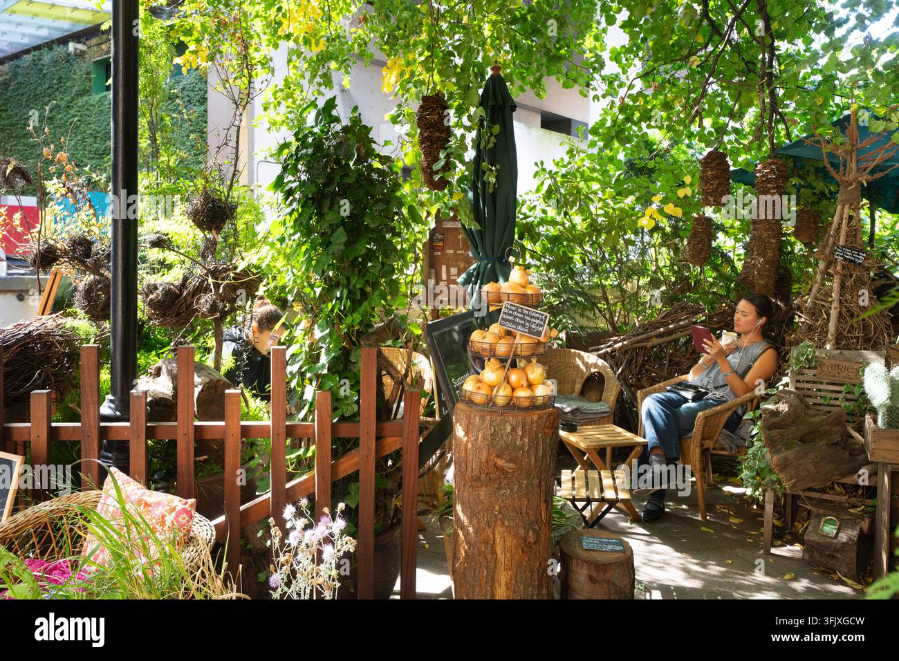 Une femme lit un liseuse électronique dans le Jardin des Oignons à London Victoria, profitant d'une évasion paisible au milieu d'une verdure luxuriante. Banque D'Images