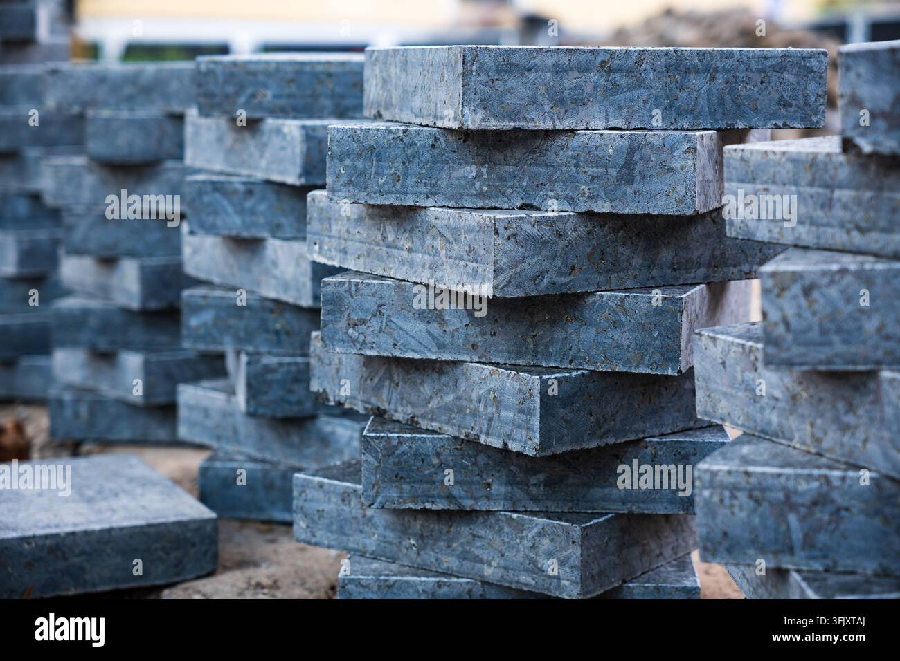 Vue rapprochée de plusieurs piles de dalles de pavage en granit gris foncé carrées et de blocs de béton prêts pour les travaux de construction de trottoirs en extérieur pendant Banque D'Images