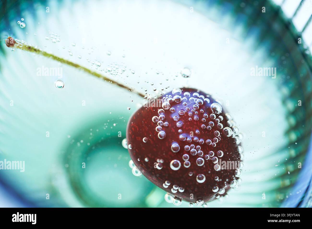 Cerise flottante avec bulles pétillantes dans un verre en cristal macro Banque D'Images