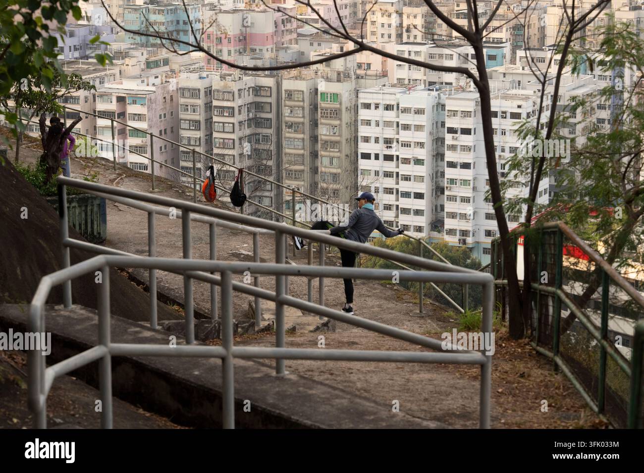 Un sportif s'étire sur un sentier de Beacon Hill à Sham Shui Po, Hong Kong, en utilisant une rampe pour sa forme physique avec vue sur des immeubles d'habitation denses. Banque D'Images