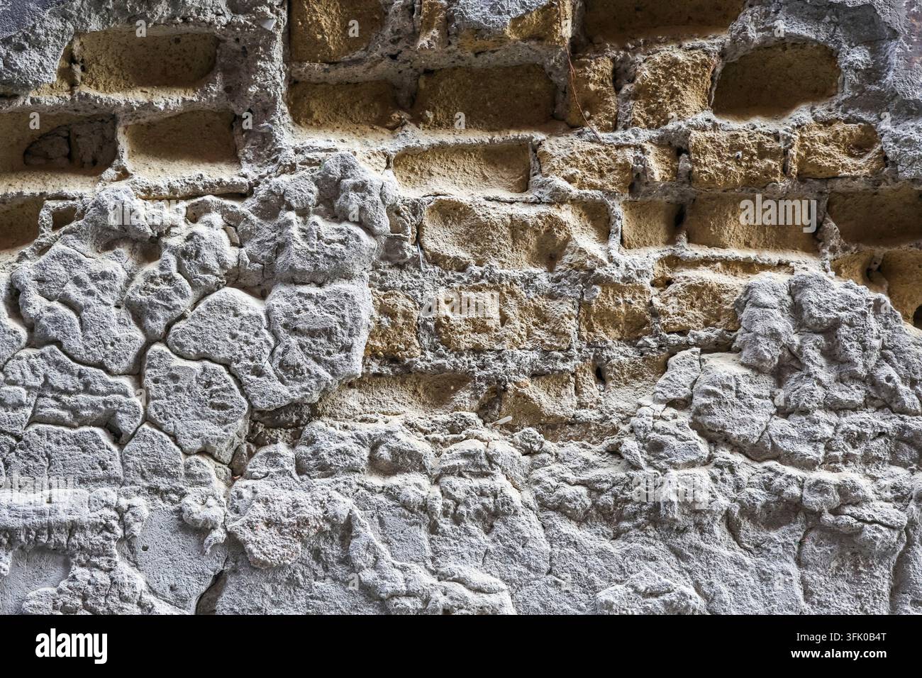 Vieux mur de briques montrant une surface de plâtre détériorée et des briques jaunes exposées Banque D'Images
