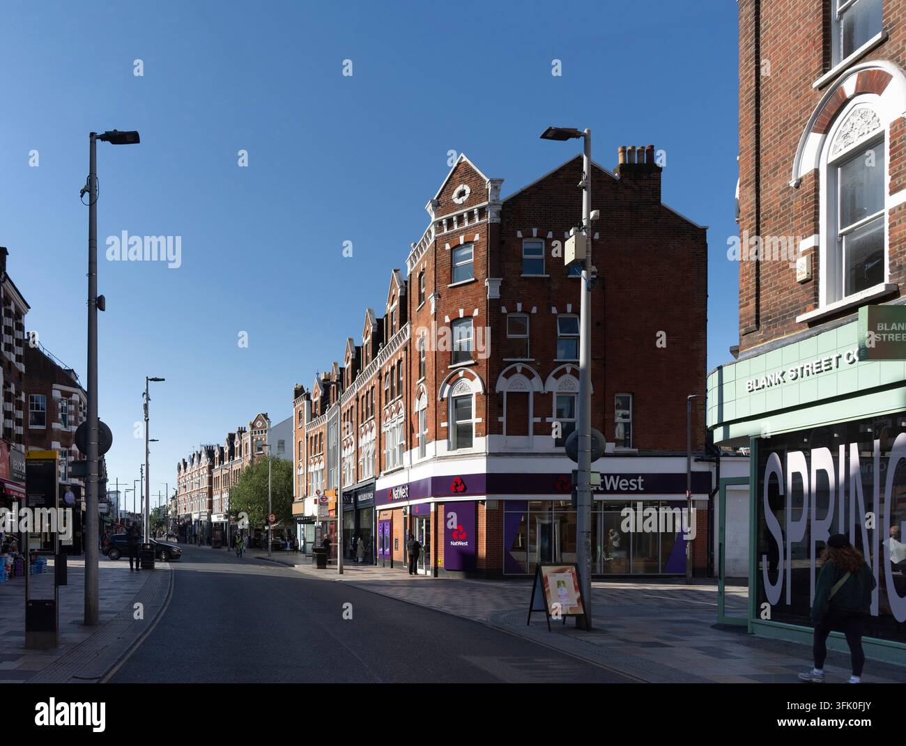 Les piétons déambulent le long de St. John's Hill à Clapham Junction, Londres, passant devant des magasins et l'angle de la banque NatWest par une journée lumineuse et ensoleillée. Banque D'Images