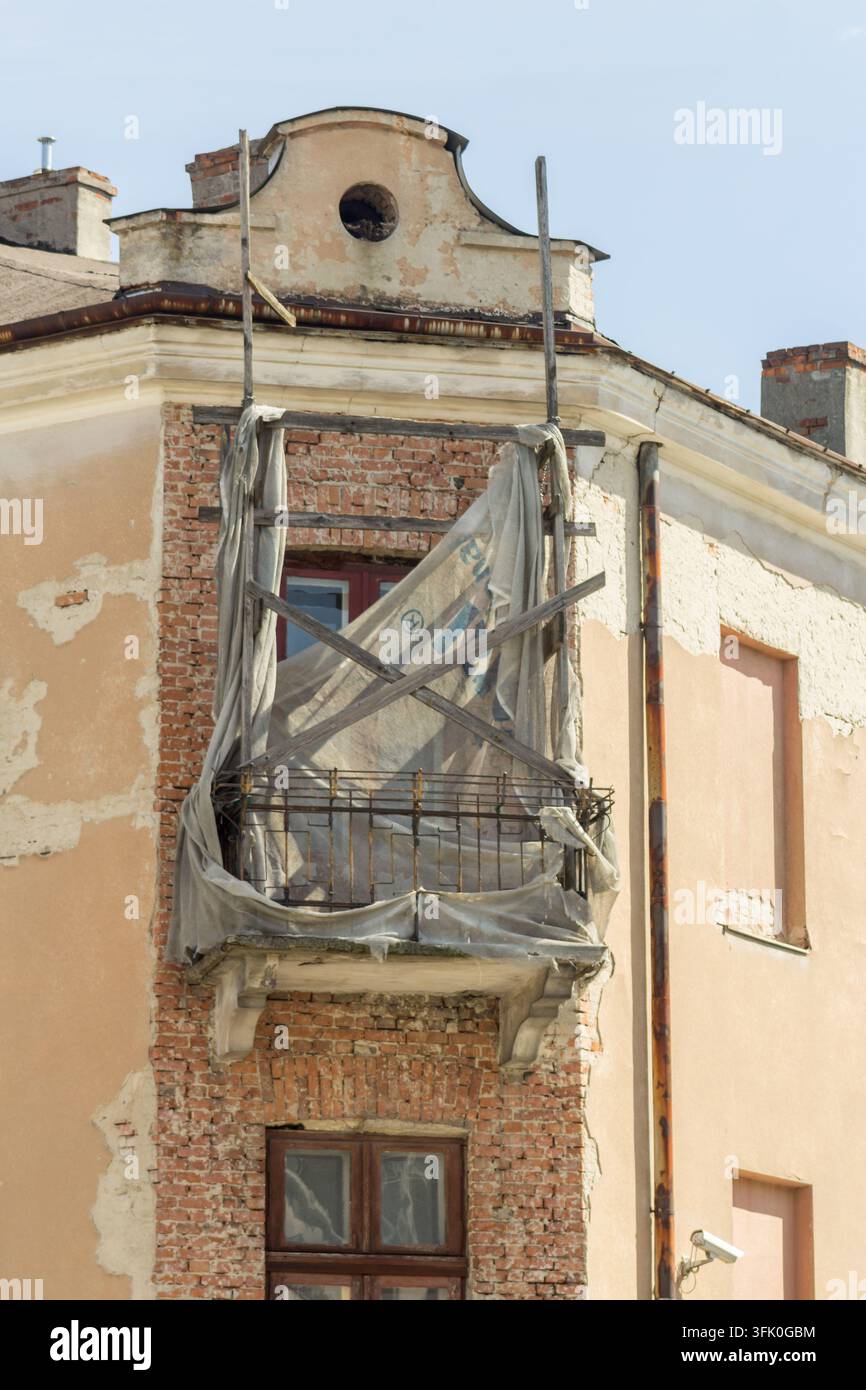 Façade historique érodée avec un balcon endommagé, maçonnerie apparente, enduit écaillé et supports métalliques. Banque D'Images