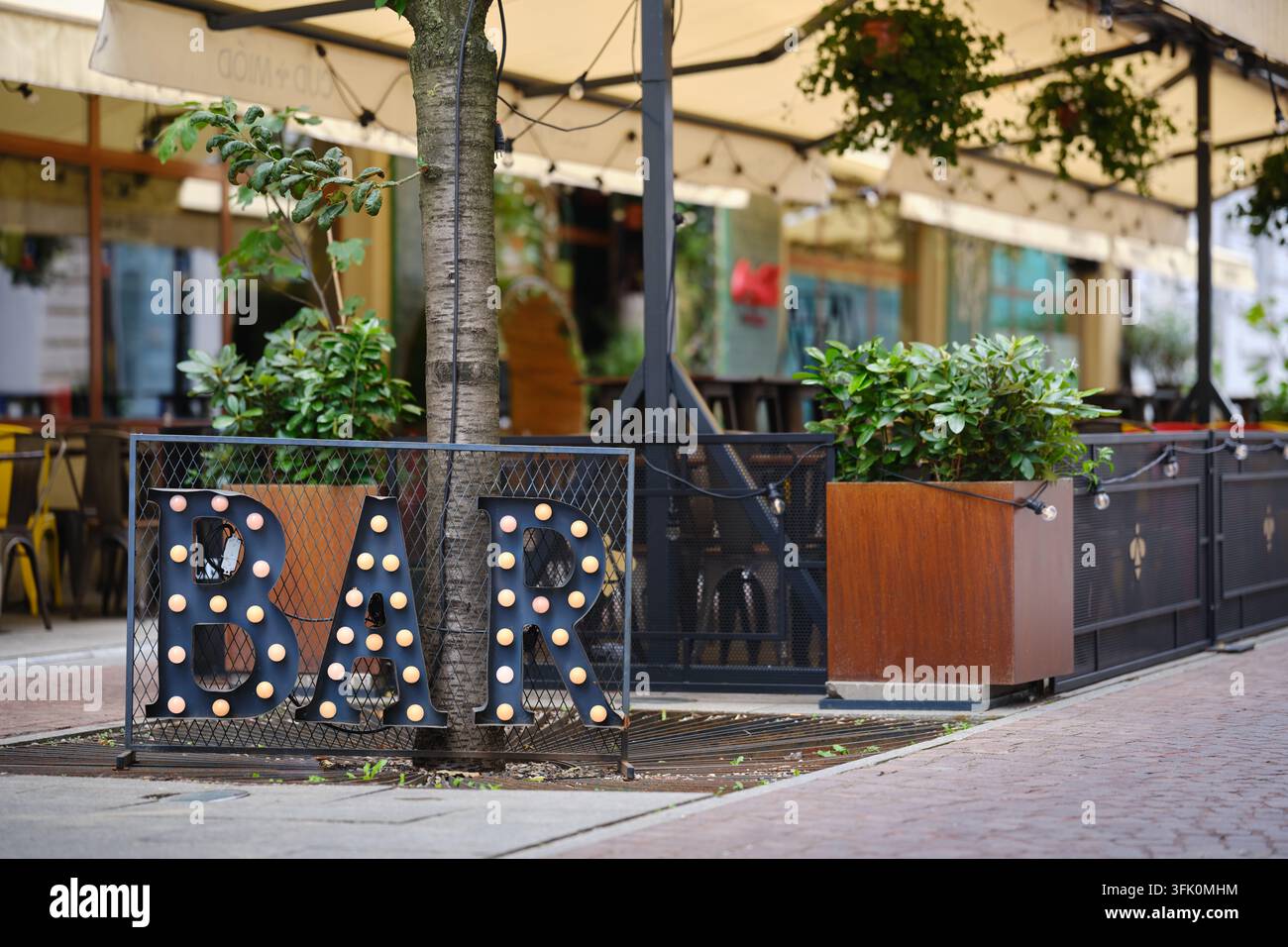 Panneau BAR illuminé devant une terrasse de restaurant extérieur avec des plantes et des sièges, montrant l'hospitalité urbaine et les loisirs. Banque D'Images