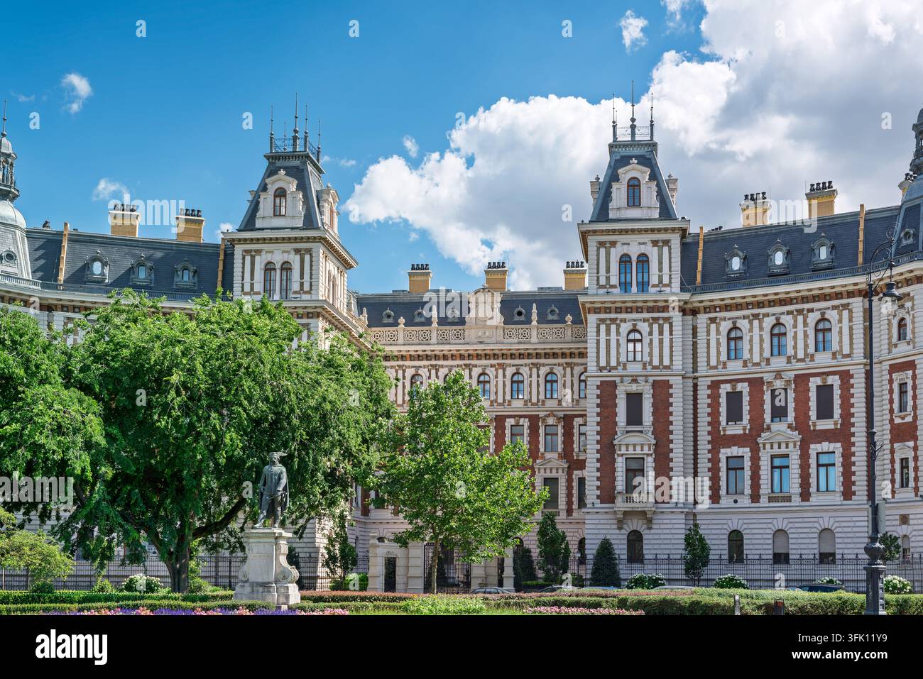 Des toits mansardés abrupts et des tours à pinacles couronnent une longue façade en brique rouge et pierre crème d'un ancien palais d'administration ferroviaire, une statue en bronze et Banque D'Images