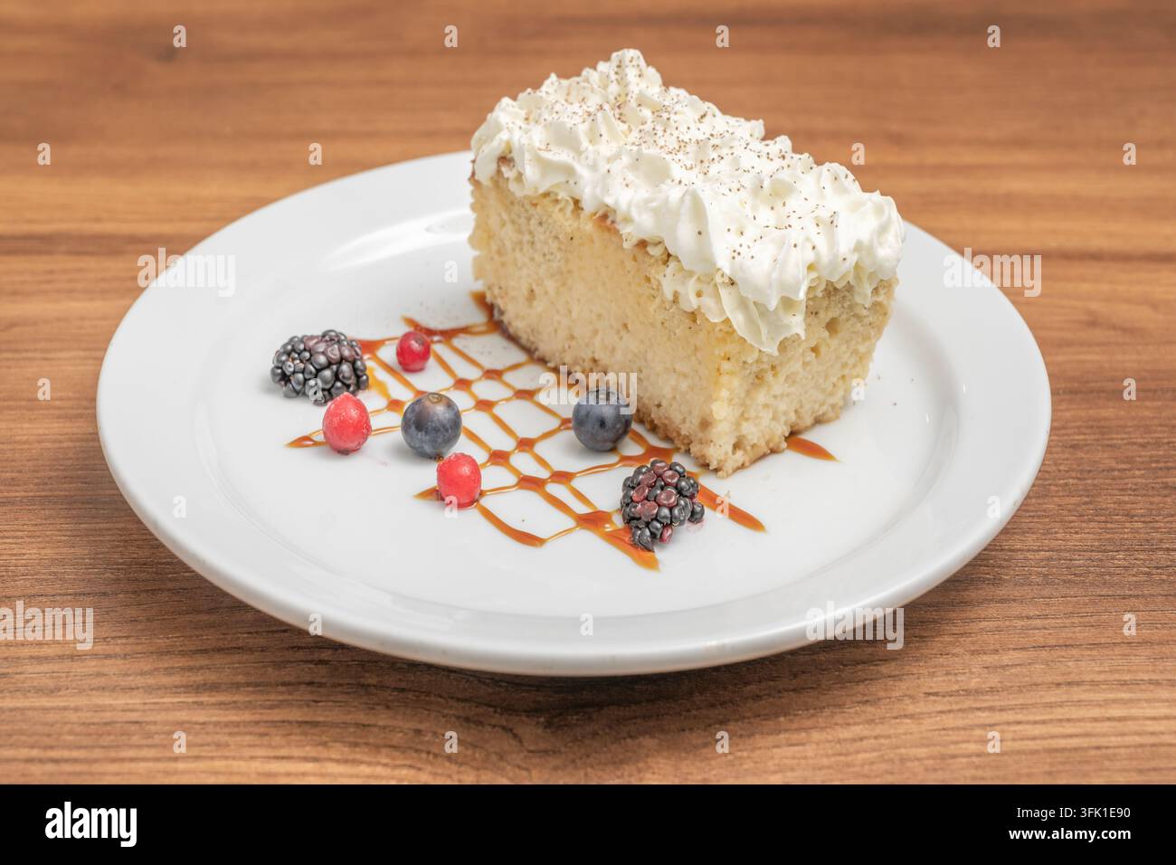 Tranche de gâteau éponge garnie de crème fouettée et de copeaux de chocolat, servie avec des fruits rouges et une sauce au caramel dans une assiette blanche. Banque D'Images
