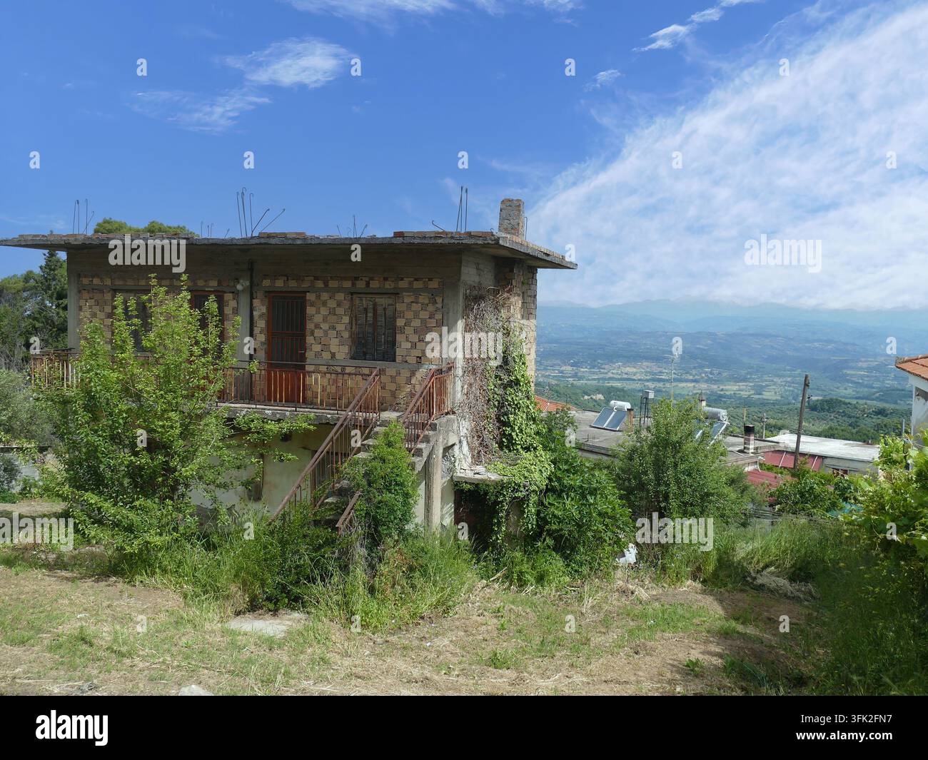 Maison inachevée avec des barres d'armature exposées et une végétation envahissante sur une colline dans un village rural près d'Olympie, en Grèce, offrant des vues panoramiques sur la di Banque D'Images