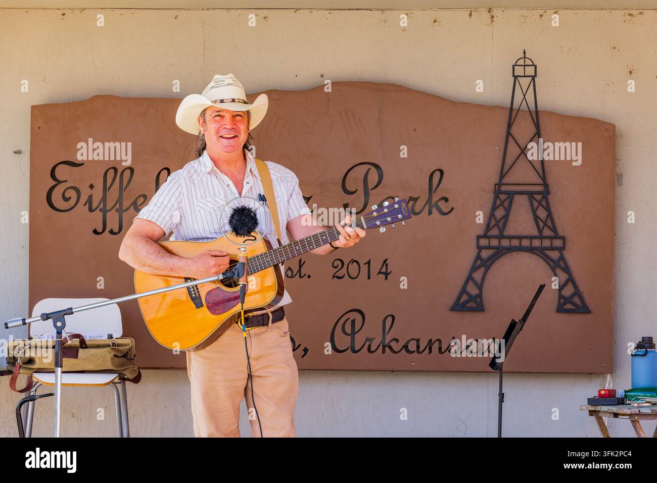 Arkansas, États-Unis, 07 AVR 2024 - Un homme heureux portant un chapeau de cowboy joue une guitare acoustique en plein air devant un panneau décoratif pour Eiffel Banque D'Images