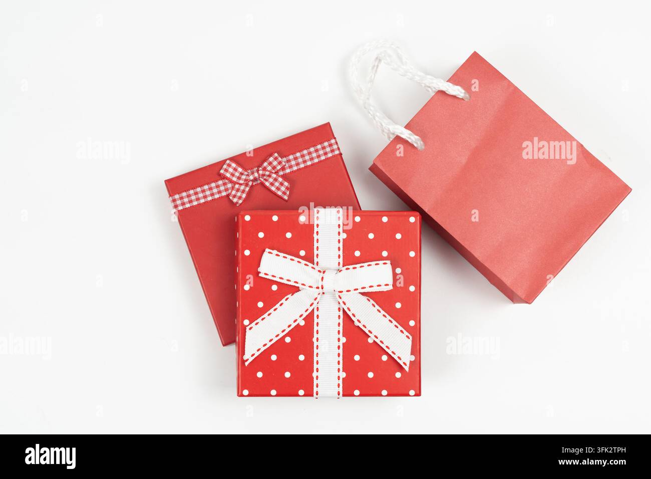 Flat lay de boîtes cadeaux rouges avec nœuds décoratifs à côté d'un sac de courses en papier sur fond blanc. Idéal pour Noël, la Saint-Valentin et les ventes de vacances Banque D'Images