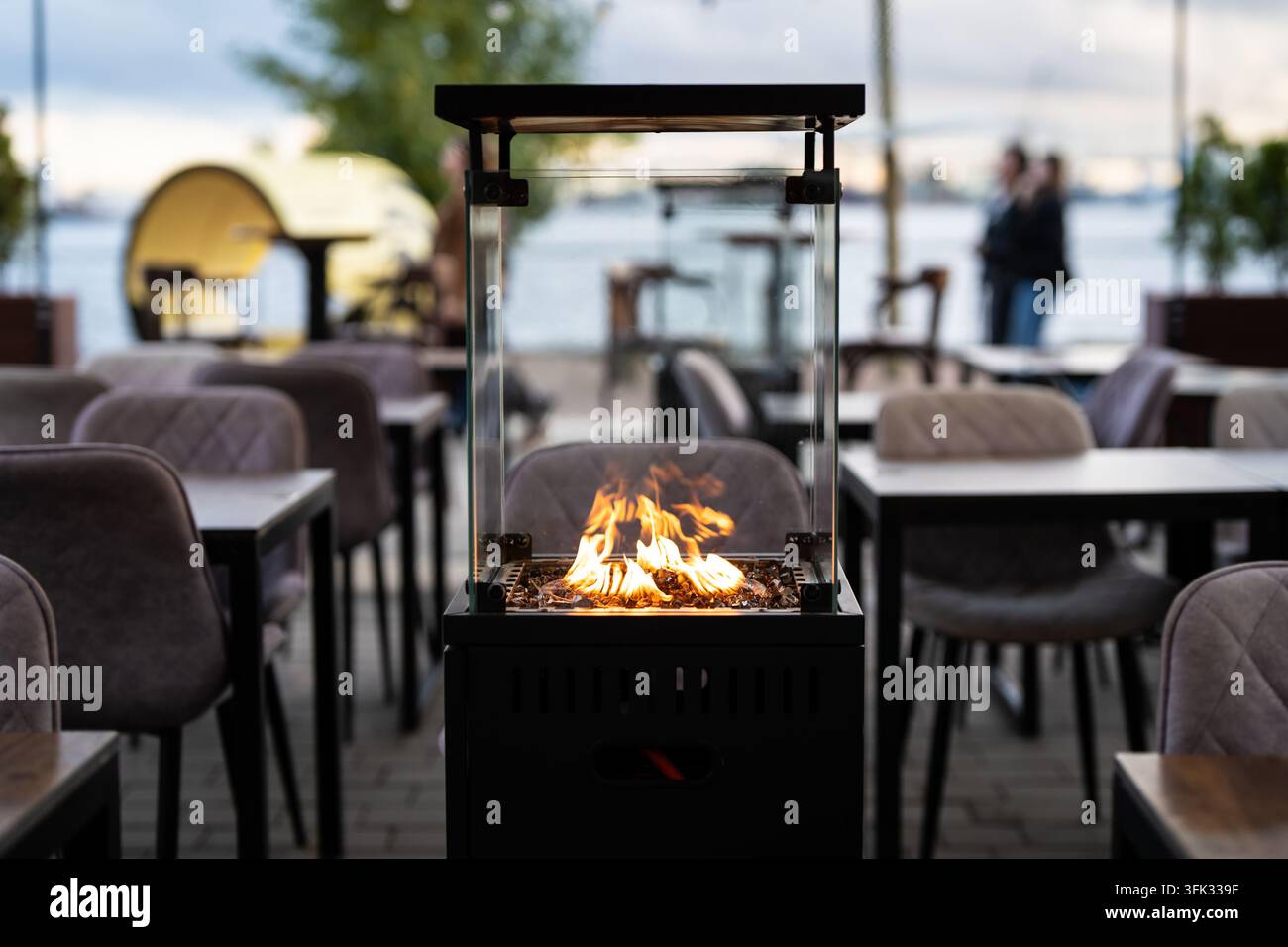 Cheminée à gaz enclose de verre réchauffant la terrasse extérieure d'un restaurant par temps froid d'automne Banque D'Images