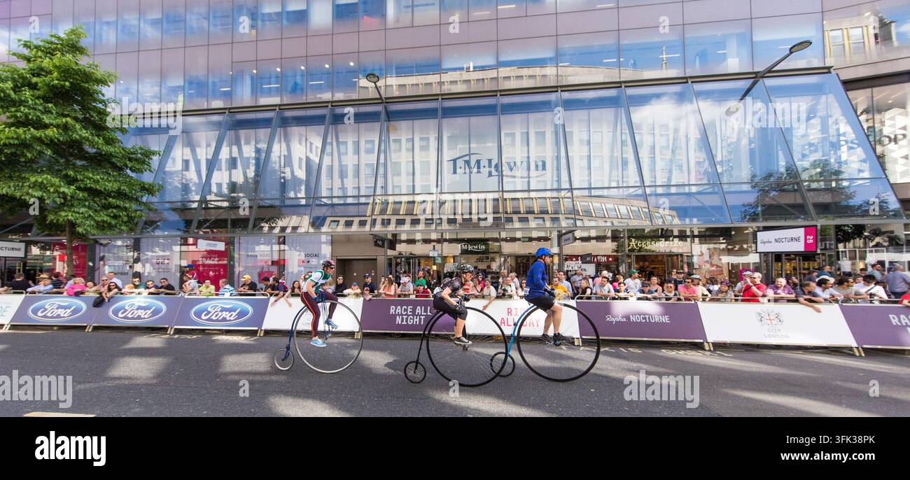 Les cyclistes courent au penny-farthings au London nocturne, en passant devant l'emblématique bâtiment One New change dans la City de Londres. Banque D'Images
