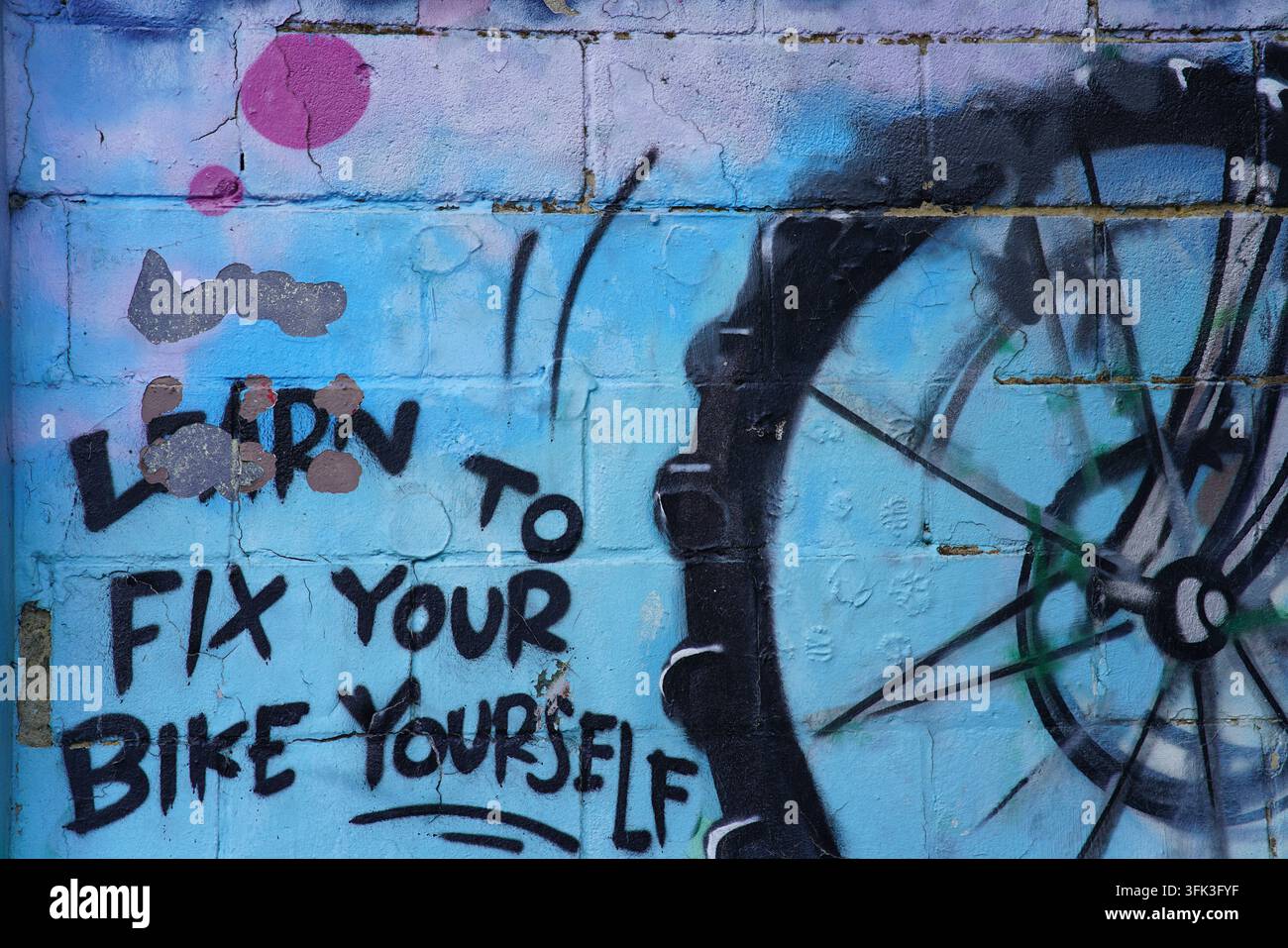 Graffiti portant l'inscription "Apprenez à réparer votre vélo vous-même" à côté d'une roue peinte sur un mur bleu à Brighton, en Angleterre. Banque D'Images