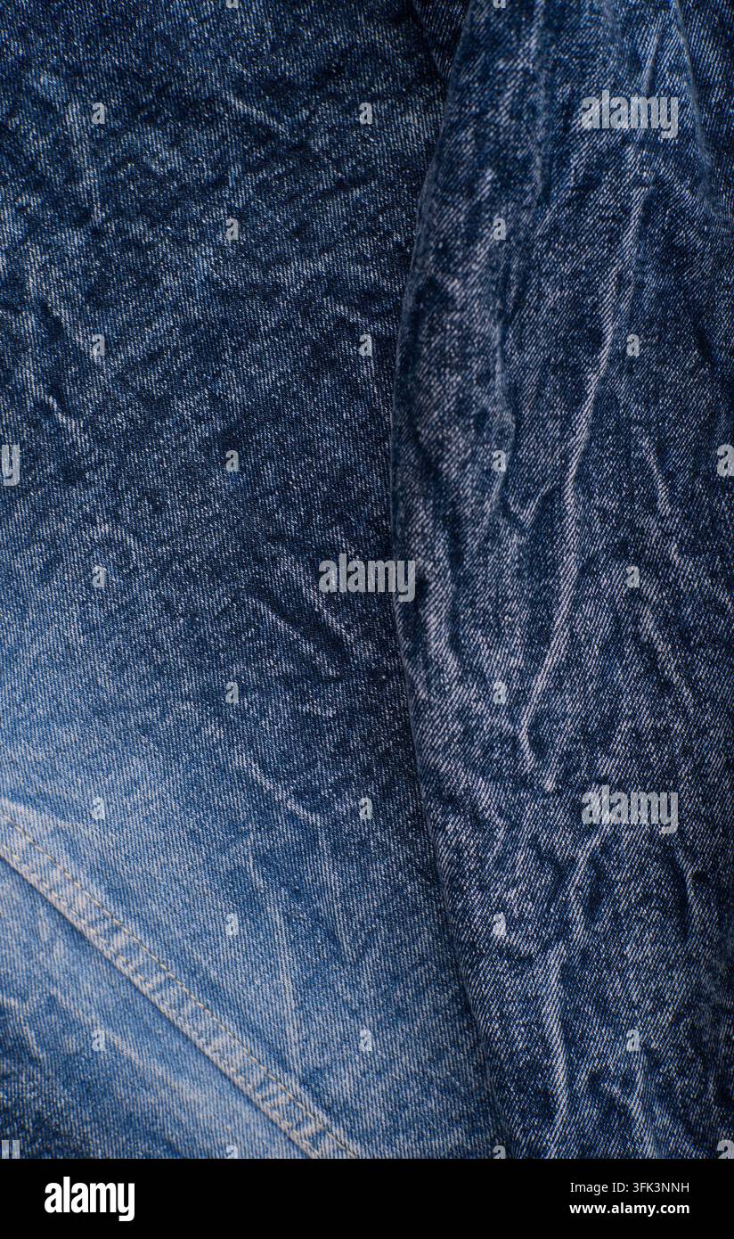 Texture textile en denim bleu verticale avec des zones délavées, des coutures et des détails de surface textile robuste. Banque D'Images