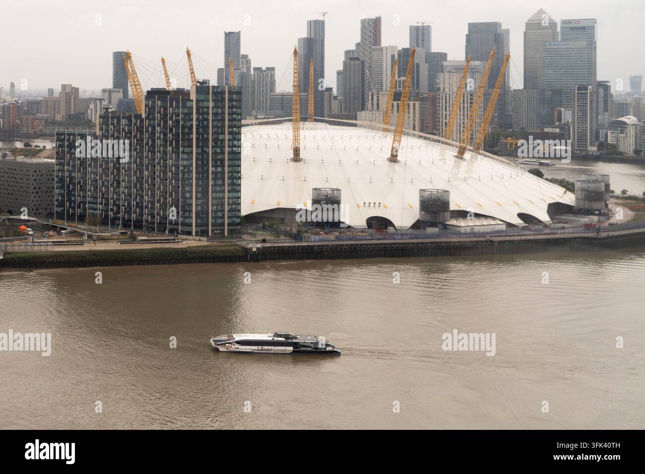 Une ferry Uber Boat navigue sur la Tamise devant l'O2 Arena à Greenwich, Londres, avec la skyline de Canary Wharf en arrière-plan. Banque D'Images