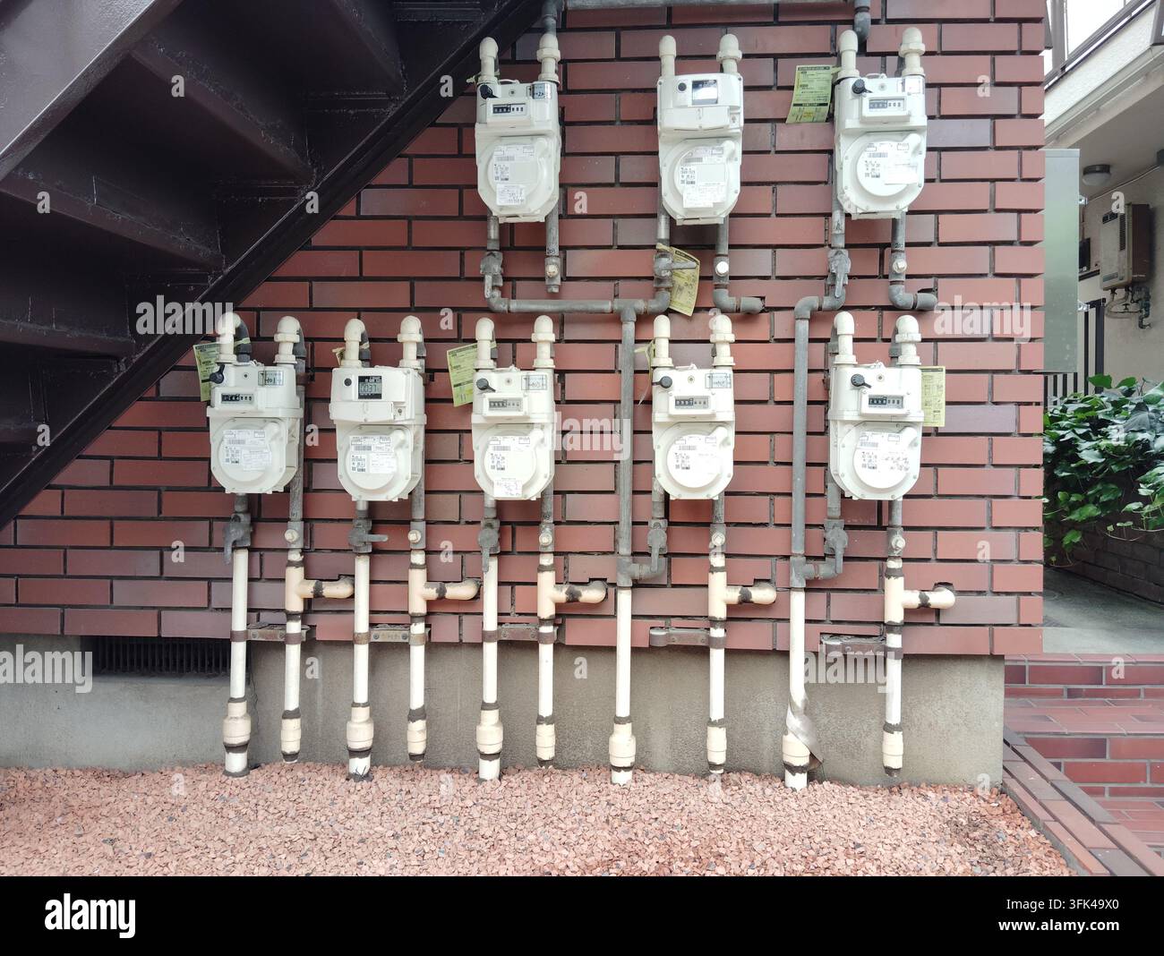 Plusieurs compteurs de gaz et tuyaux de service exposés disposés sur le mur extérieur en briques d'un immeuble d'habitation à Tokyo, Japon. - Image de stock capturée avec un smartphone