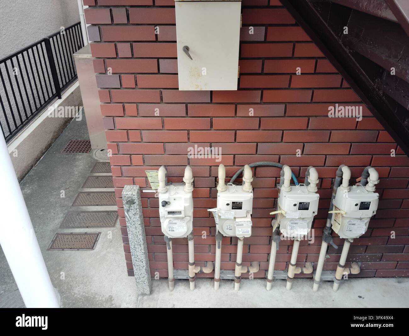 Quatre compteurs de gaz et des tuyaux exposés installés sur le mur extérieur en brique d'un immeuble résidentiel à Tokyo, Japon. - Image de stock capturée avec un smartphone