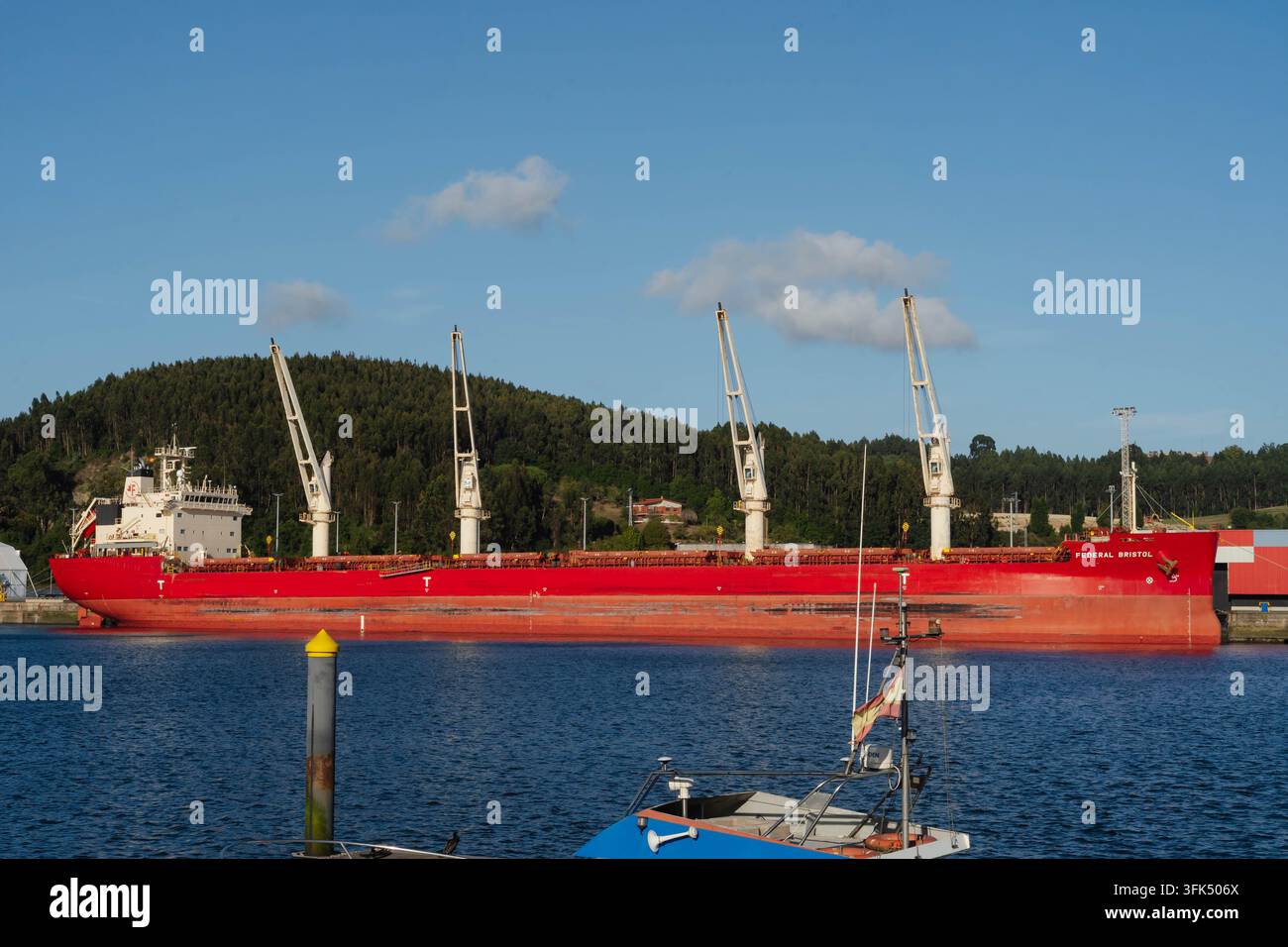 Aviles, Espagne – 20 septembre 2026 Un porte-conteneurs rouge est amarré au quai de l'estuaire avec les grues de pont surélevées au-dessus des cales. Transport maritime de marchandises et sec Banque D'Images