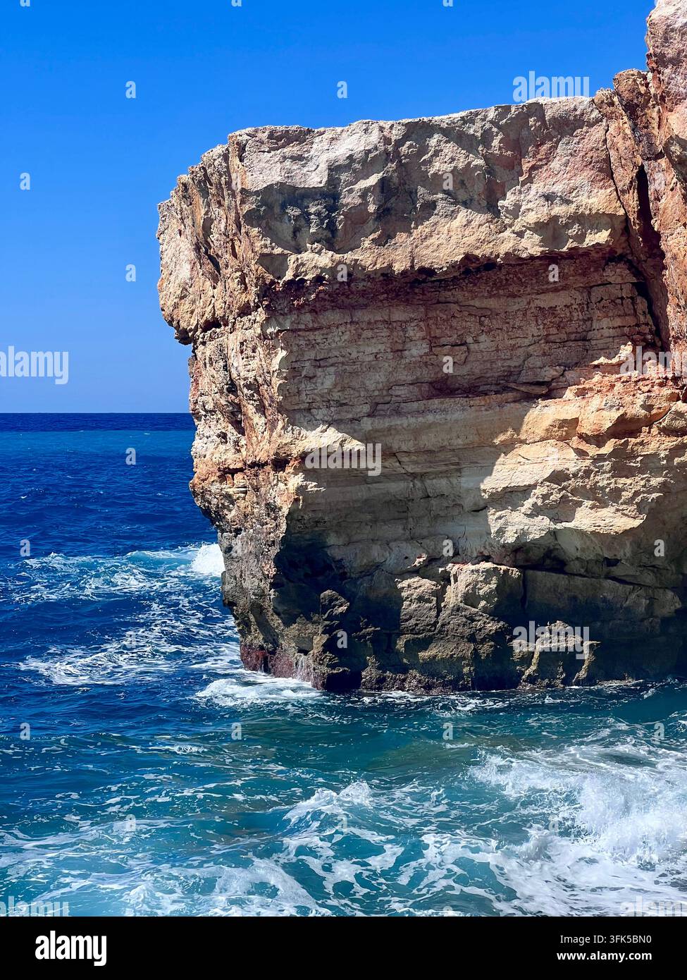 Formation rocheuse en calcaire stratifiée qui émerge dramatiquement de la mer bleu profond à la plage de Spilies, Crète, Grèce - Image de stock capturée avec un smartphone