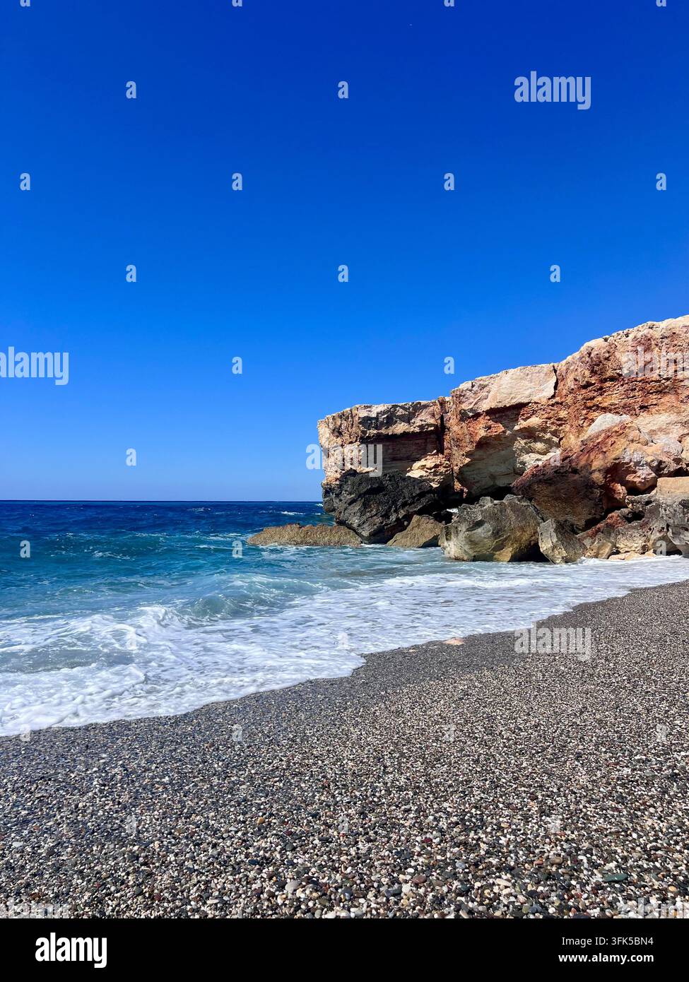Plage de galets tranquille avec des falaises rocheuses stratifiées dramatiques et des vagues turquoise venant s'échouer à la plage de Spilies, Crète, Grèce. - Image de stock capturée avec un smartphone
