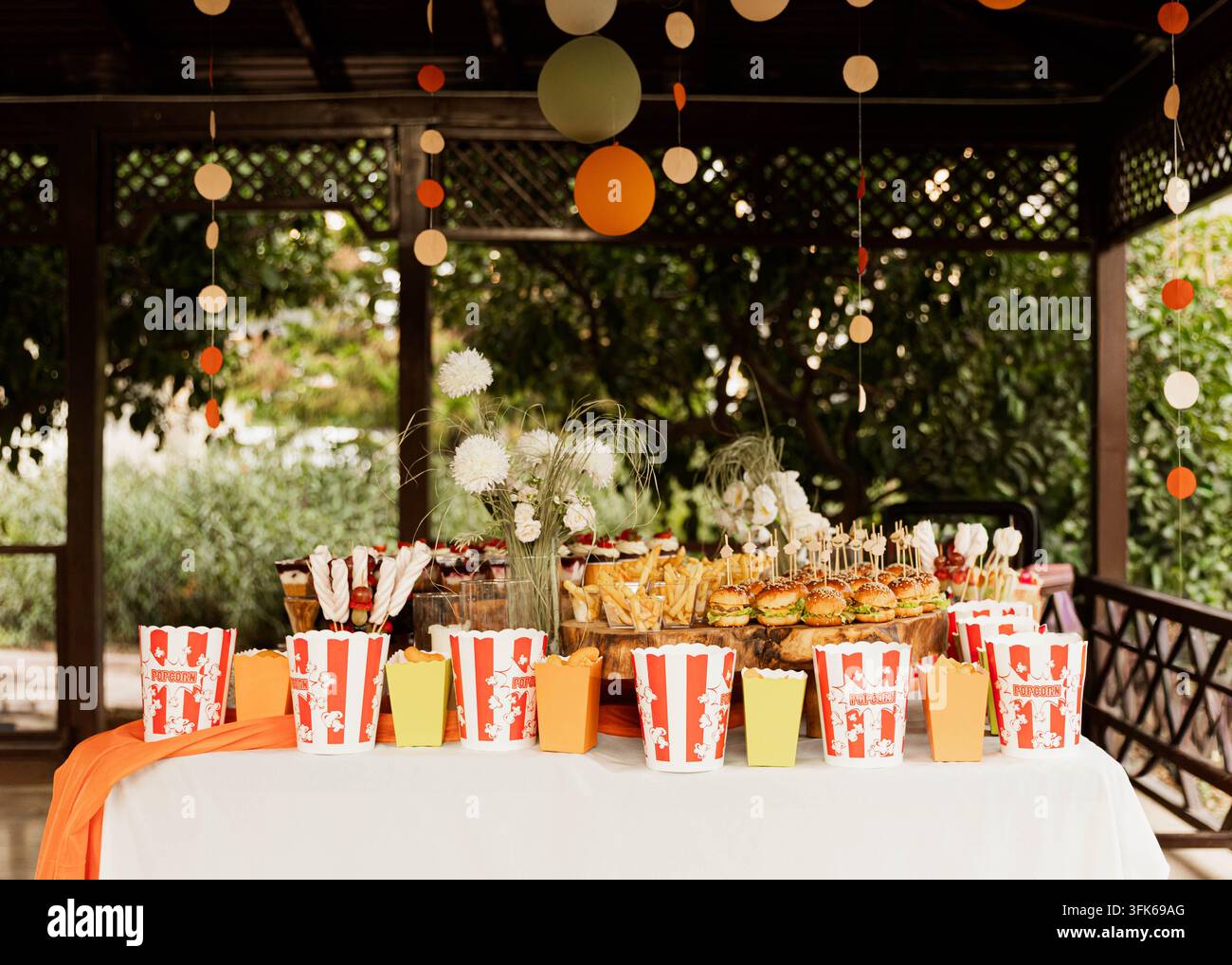 Table de nourriture pour fête en plein air avec des boîtes à popcorn rayées, des snacks variés et des décorations suspendues arrangées pour une célébration ou un événement traité par un traiteur. Banque D'Images