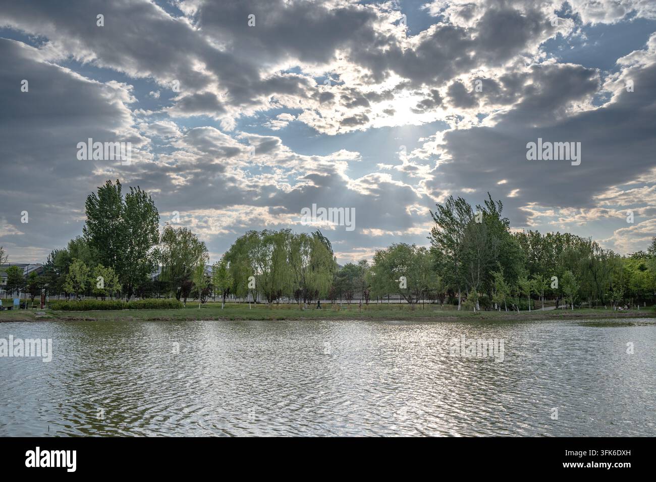 La lumière du soleil traversant les nuages au-dessus de l'eau ondulante d'un lac dans un parc Banque D'Images