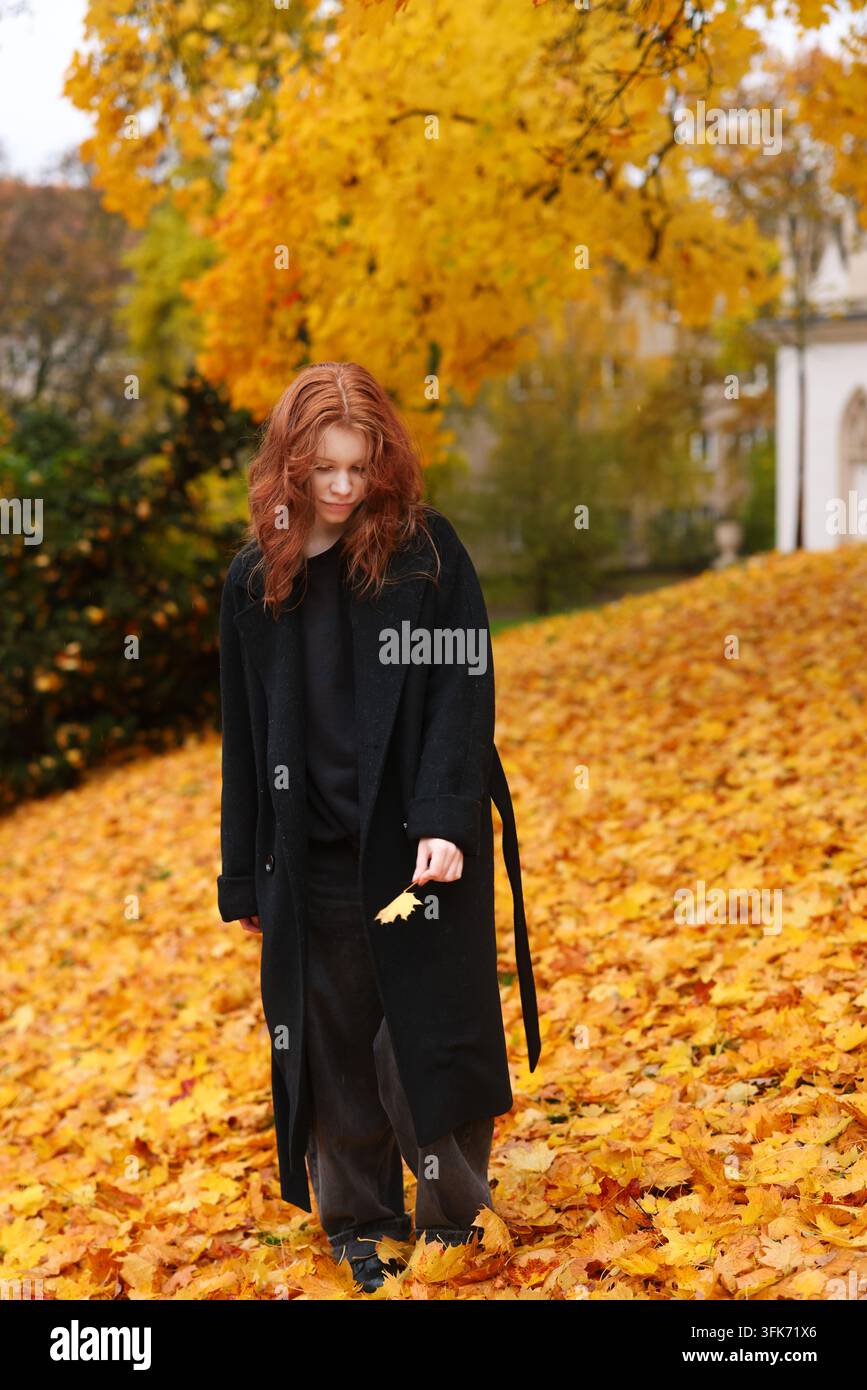 Femme rousse marchant en montée à travers des feuilles d'automne dorées, illustrant la croissance personnelle, la persévérance et le changement saisonnier. Banque D'Images