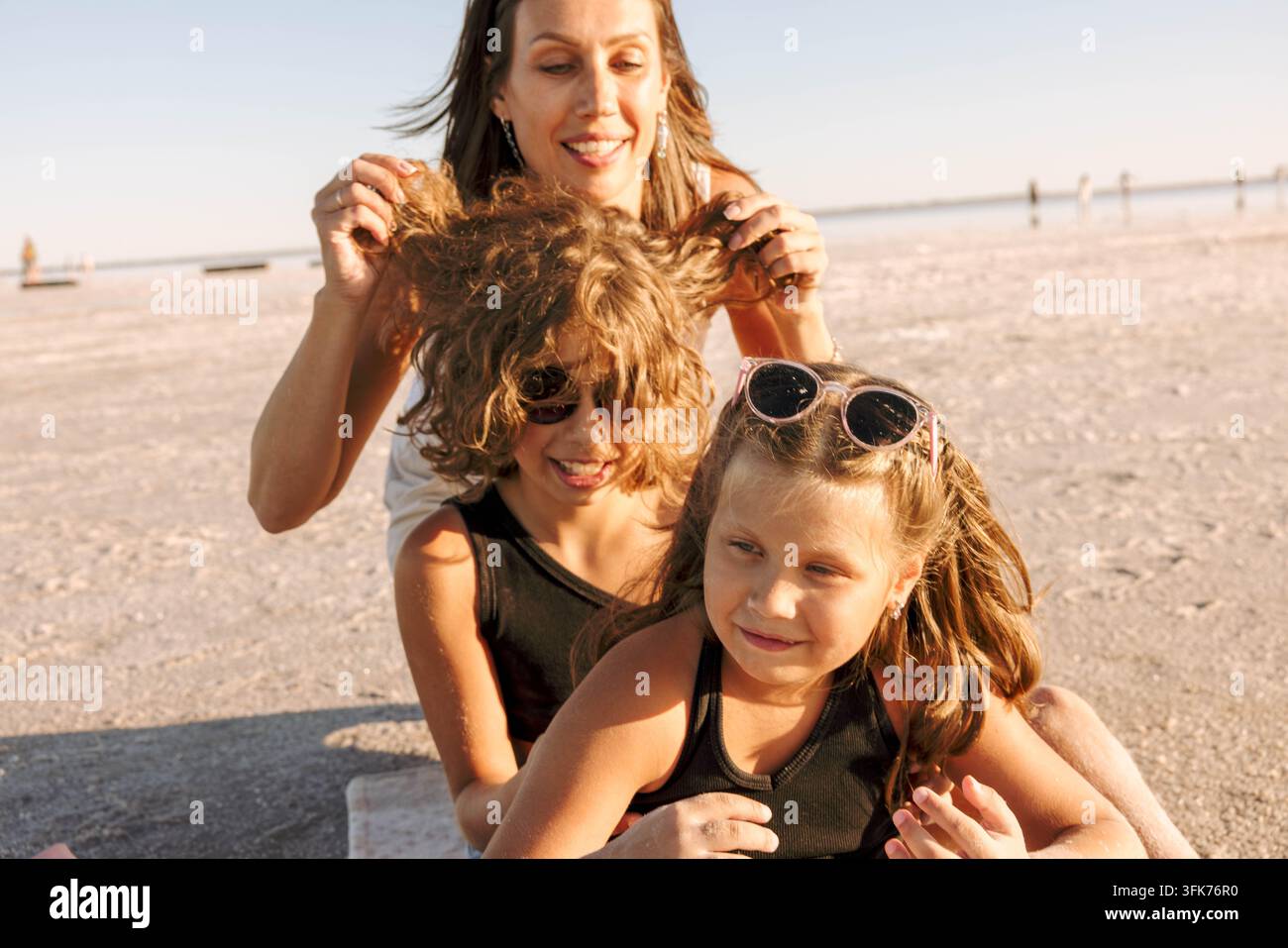 Mère heureuse riant avec ses deux filles espiègles, vacances familiales relaxantes au lac de sel rose, soleil de l'heure dorée, émotions authentiques et Banque D'Images