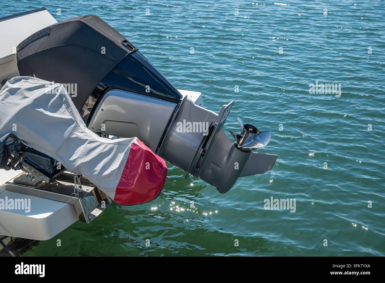 Vue rapprochée d'un moteur hors-bord sorti avec hélice exposée au-dessus de l'eau dans une marina. Banque D'Images