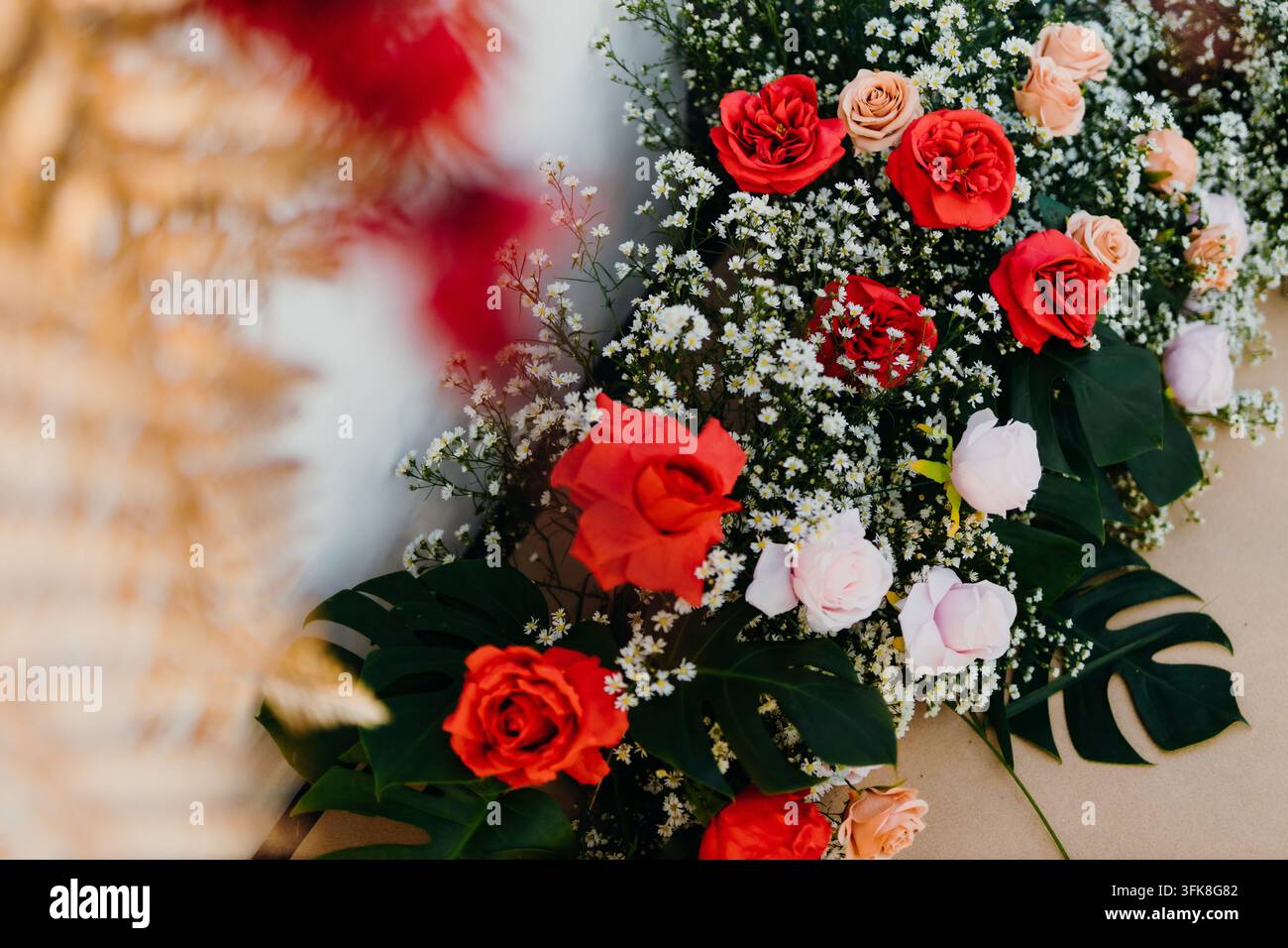 Arrangement floral élégant de mariage avec des roses rouges et des fleurs pastel sur des feuilles de monstera Banque D'Images