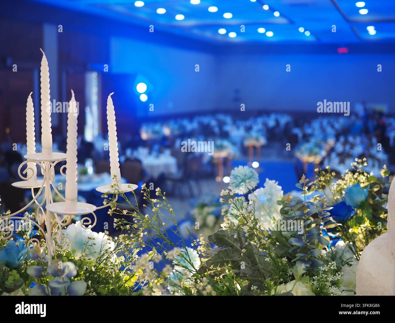 Élégants candélabres blancs et centres de table floraux lors d'une réception de mariage dans un salon de bal éclairé en bleu Banque D'Images