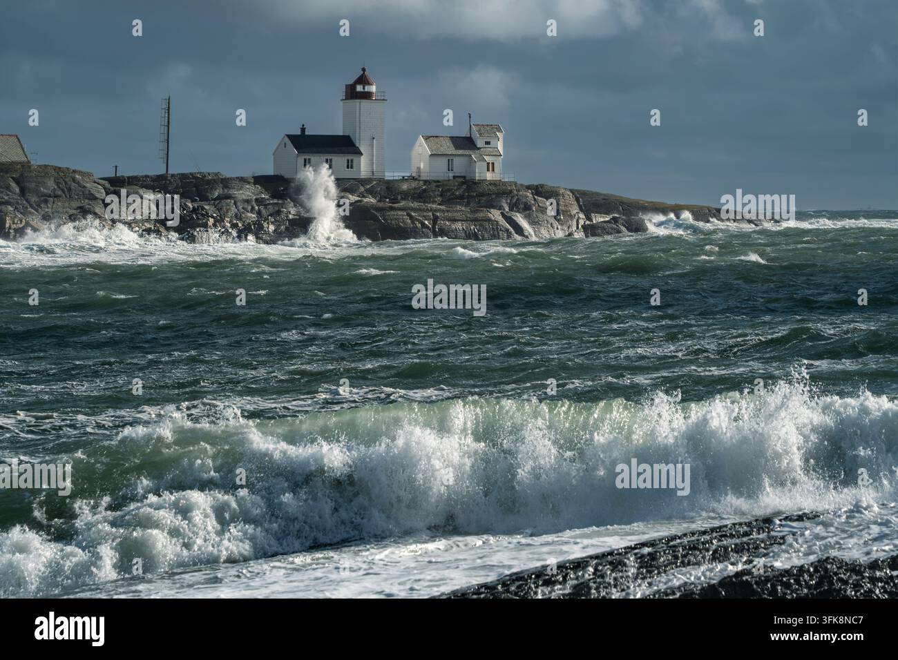 La profondeur à travers les couches de tempête relie une vague se brisant au premier plan, l'eau verte rugueuse et le phare de Langoytangen en Norvège pour une puissance côtière, une histoire météorologique Banque D'Images