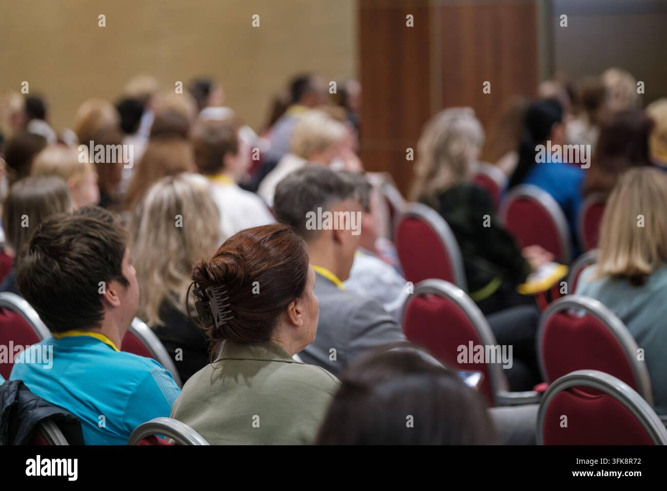 Les participants au séminaire sont assis sur des rangées de chaises rouges, deux participants étant vus de dos au premier plan. Banque D'Images