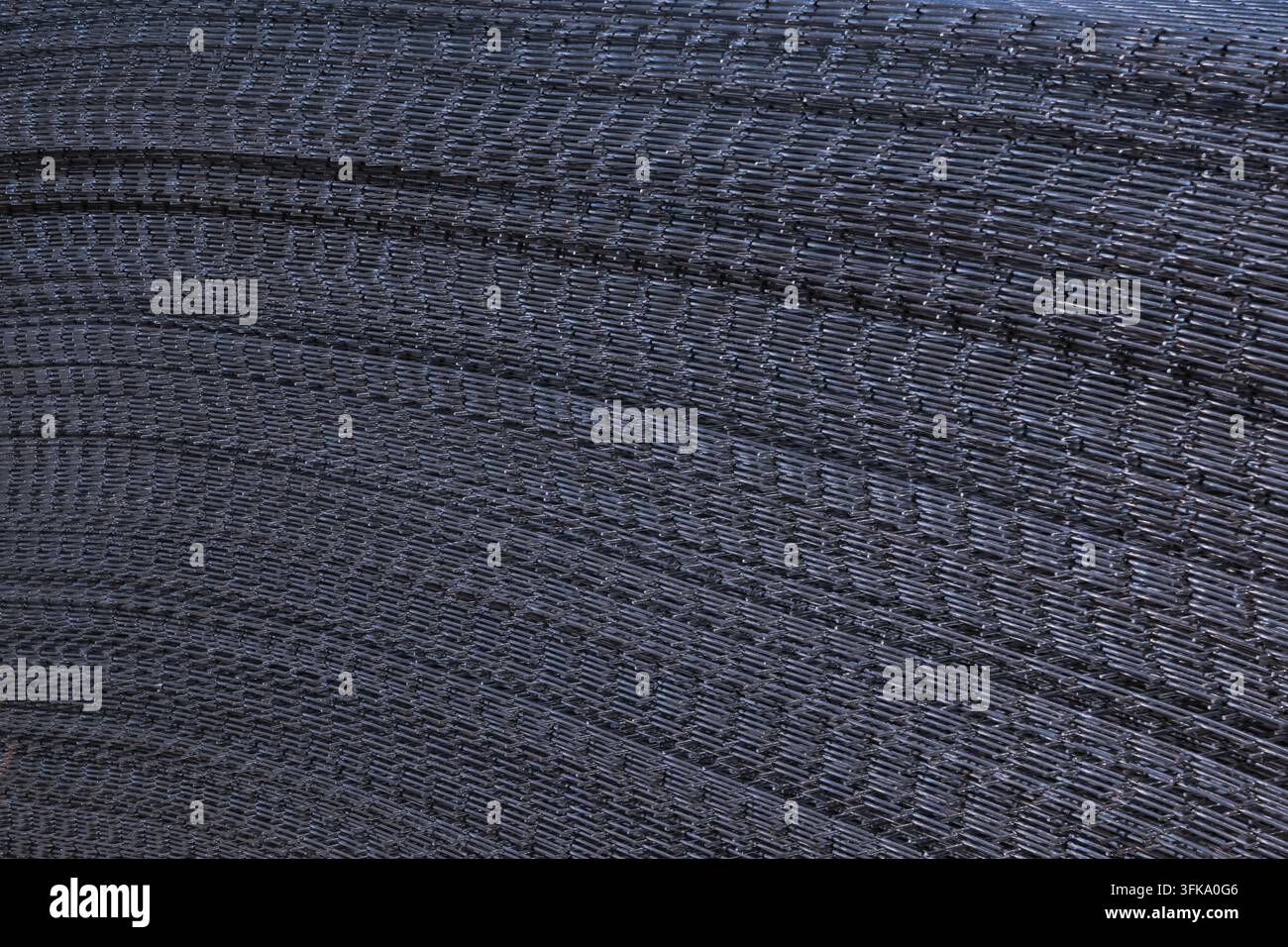 Vue rapprochée abstraite de panneaux de treillis en acier galvanisé empilés créant un motif métallique courbé à l'extérieur sur un chantier de construction. Banque D'Images