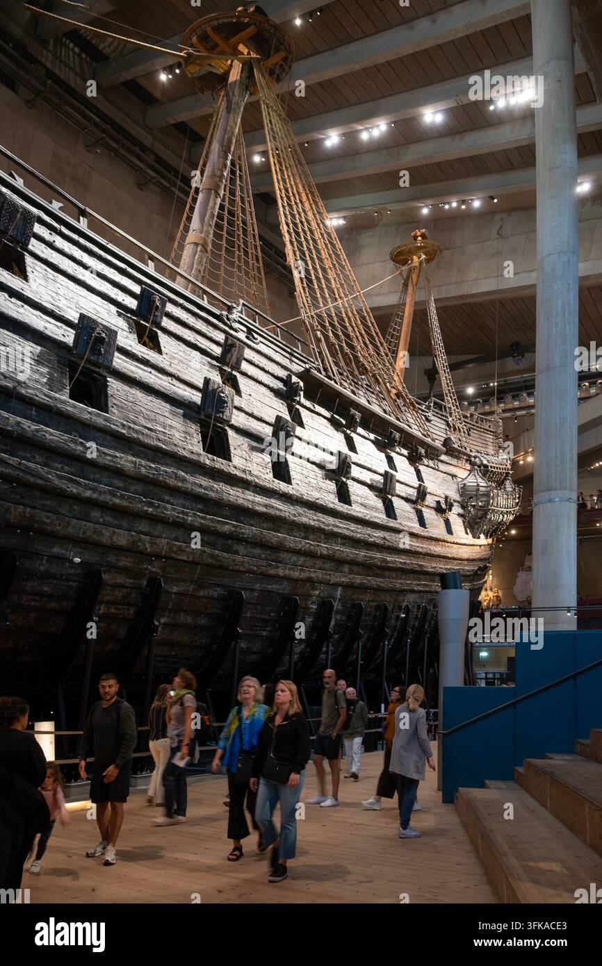 Visiteurs du musée marchant à côté de la coque massive en bois sombre et des sabords du navire de guerre Vasa du XVIIe siècle à l'intérieur du musée Vasa à Stockholm, Suède Banque D'Images