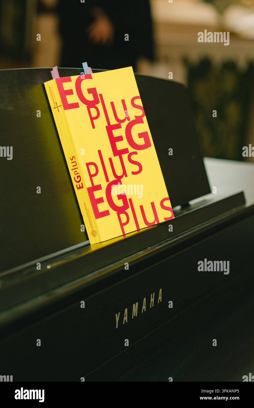 09.20.2026, Bad Hersfeld, Allemagne, Livre de chants jaune vif intitulé EG PLUS posé sur le pupitre de musique d’un piano Yamaha noir à l’intérieur d’une église. Musique d’église Banque D'Images