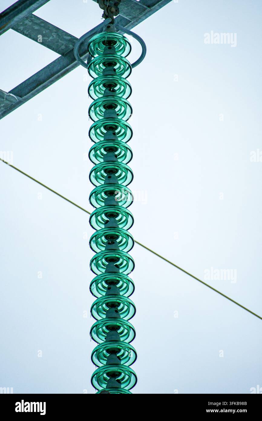 Gros plan d'une longue série d'isolateurs en verre vert sur les infrastructures de transmission d'électricité à haute tension. Banque D'Images