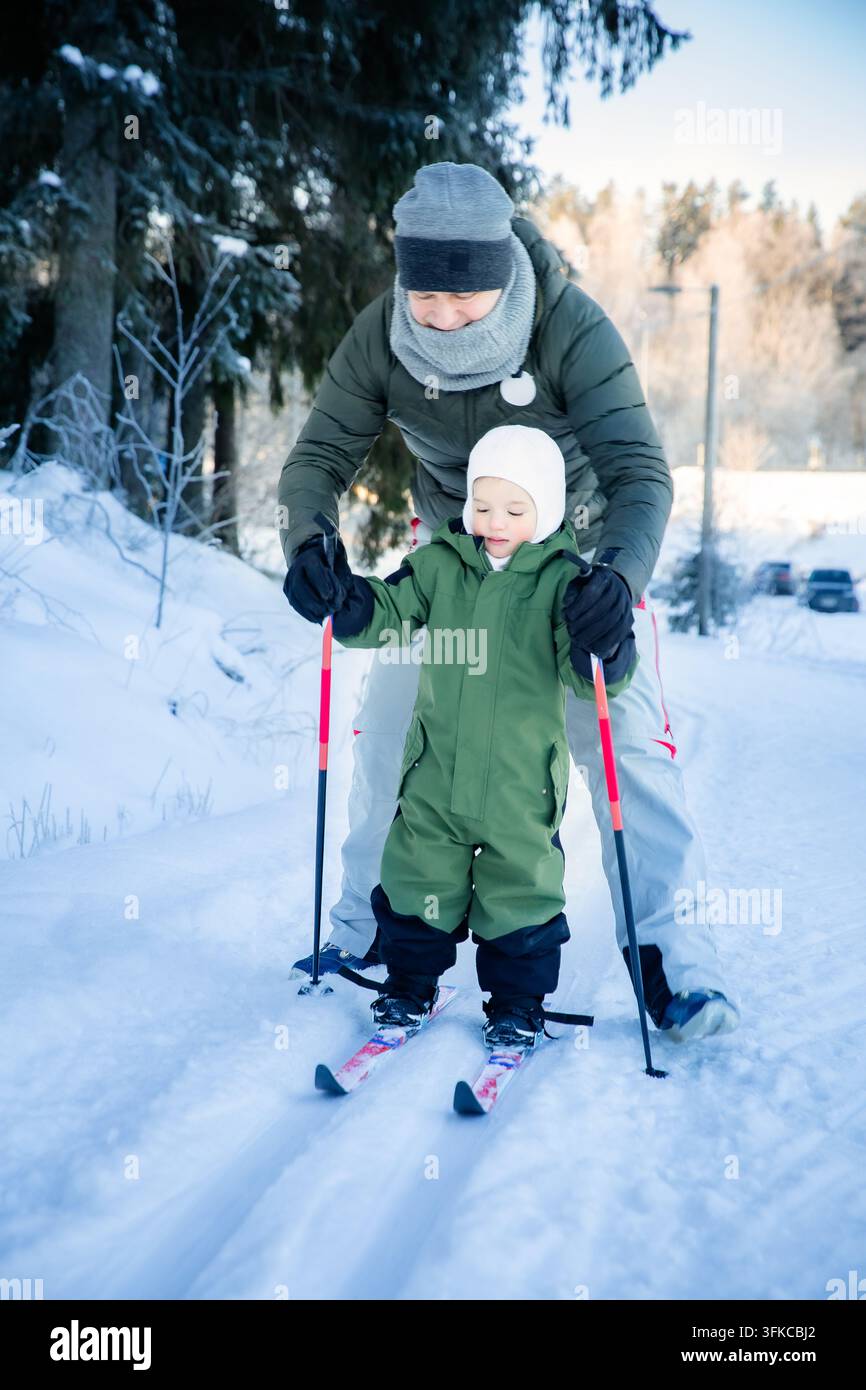 Un père aide son tout-petit à apprendre le ski de fond sur un sentier enneigé dans la région d'Helsinki, en Finlande, lors d'une sortie familiale active en hiver. Banque D'Images