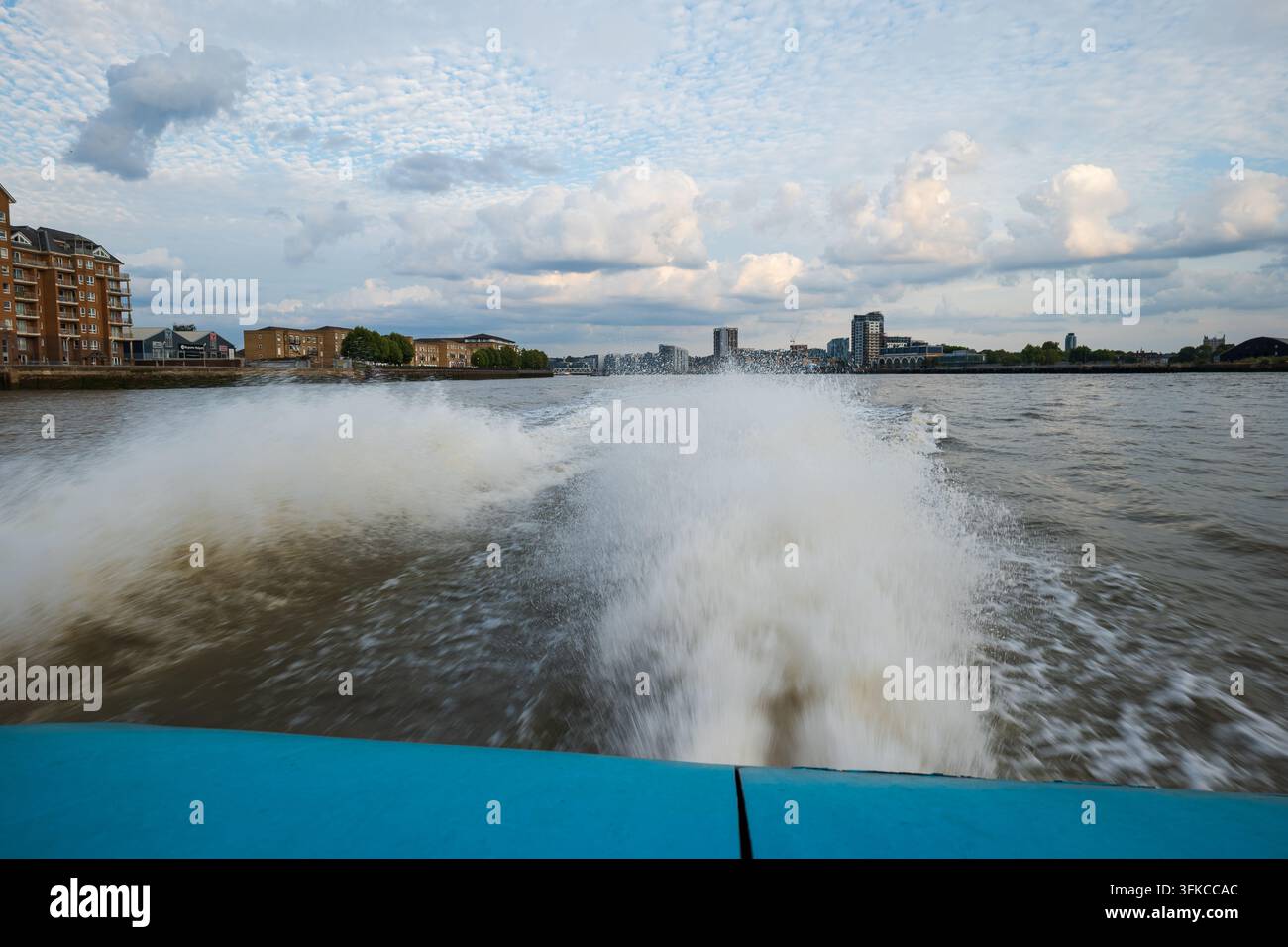 Vue depuis l'arrière d'un hors-bord regardant en arrière vers les éclaboussures d'eau blanches énergiques et le sillage d'écume tourbillonnant derrière le bateau avec un horizon urbain en arrière-plan Banque D'Images