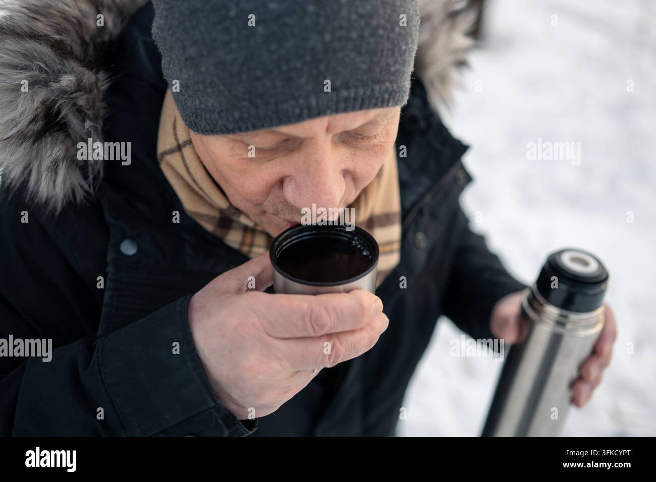 Homme mûr buvant une boisson chaude dans une tasse isotherme en hiver Banque D'Images